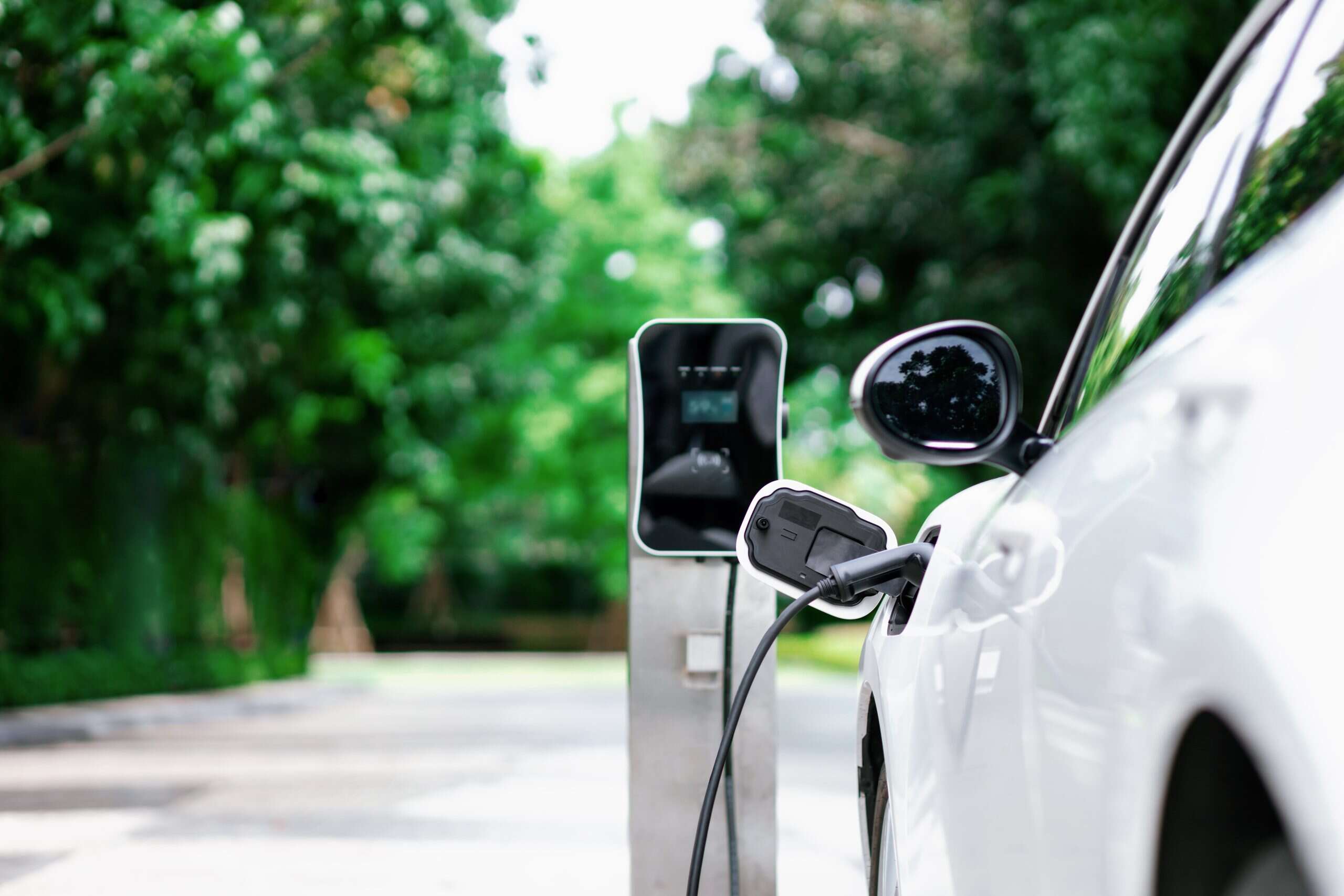 Focus closeup electric vehicle plugged in with EV charger device from blurred background of public charging station powered by renewable clean energy for progressive eco-friendly car concept.